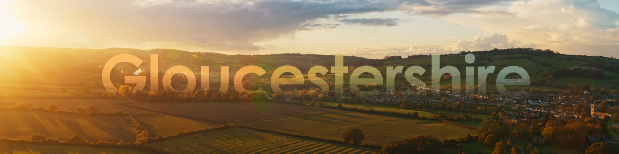 A sunset over open fields with the word Gloucestershire overlaid